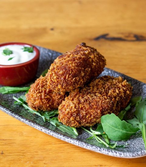 Crispy breaded chicken fillets on a plate with fresh rocket leaves and a side of creamy white dipping sauce