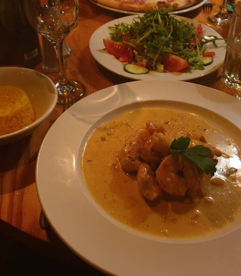 Delicious Italian meal with creamy chicken, saffron rice, fresh salad and glass of sparkling wine on a wooden table