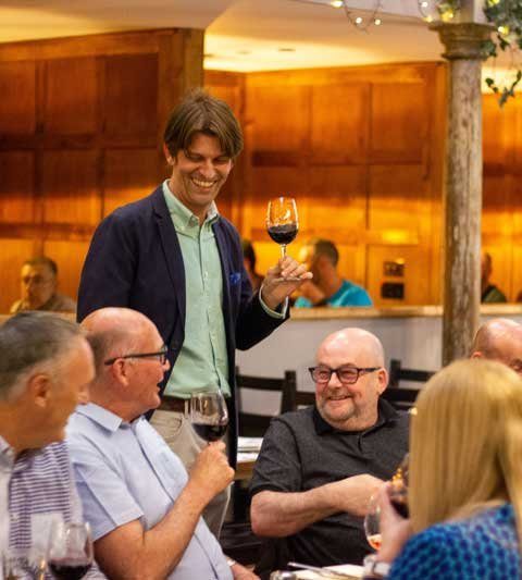 Group of people socialising at a restaurant, smiling and holding wine glasses, under warm ambient lighting