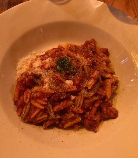 Delicious pasta dish with rich tomato sauce, topped with parmesan and herbs, served on a white plate at a cosy restaurant.