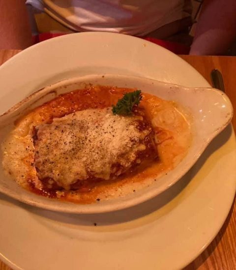 Baked lasagna with melted cheese and herbs in a ceramic dish on a wooden table setting, ready to enjoy