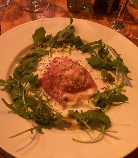 Gourmet ravioli served with creamy sauce and fresh rocket leaves on a rustic plate, perfect for fine dining enthusiasts
