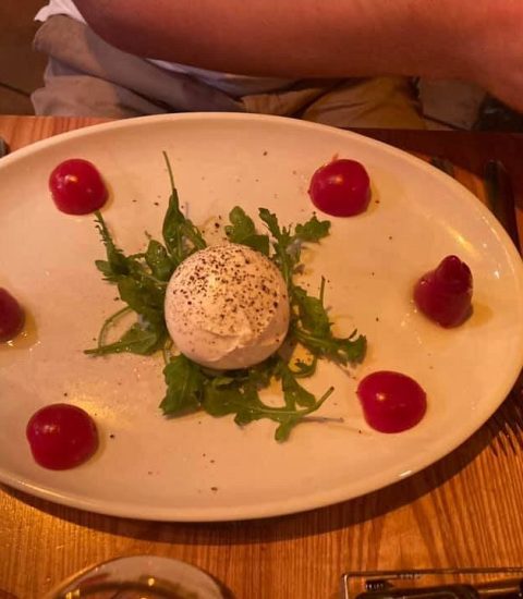Burrata cheese on a bed of rocket with sliced beets, presented on a white plate for a delicious appetiser option