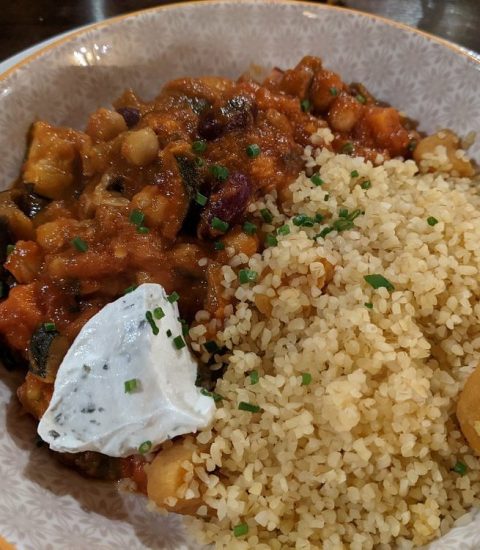 Vegetable stew with chickpeas and bulgur, topped with a dollop of cream in a patterned bowl, garnished with chives