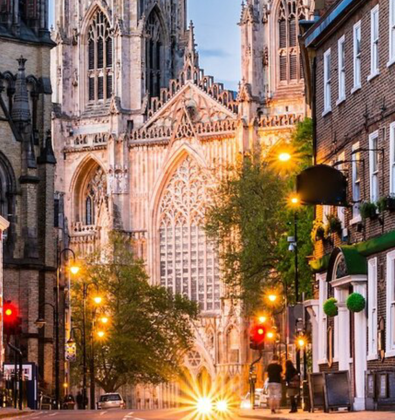 Historic cathedral lit by evening lights, street scene with pedestrians and cars, showcasing Gothic architecture in the city centre