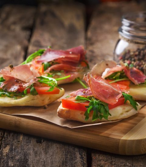 Italian bruschetta with prosciutto, tomatoes, and rocket on rustic breadboard, accompanied by a jar of pepper blend