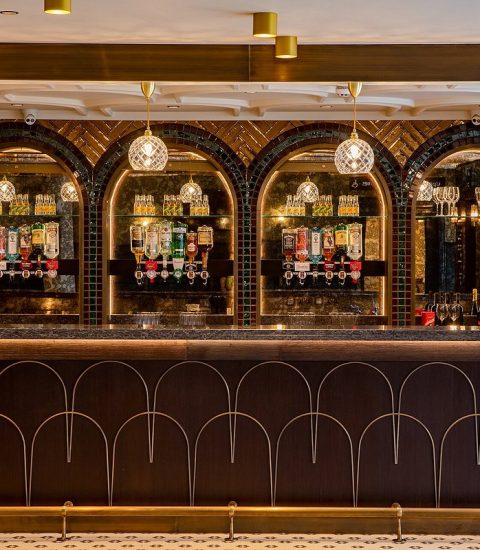 Elegant pub with ornate bar, hanging lights and diverse liquor selection, ideal for a refined social gathering ambiance