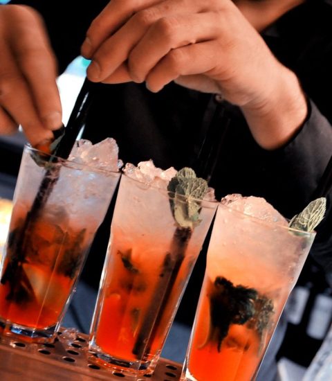 Bartender preparing three refreshing cocktails with mint and ice at a bar counter in a lively nightlife setting