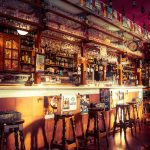 Cosy traditional pub interior with wooden bar stools and vintage decor, showcasing a variety of drinks and warm ambient lighting