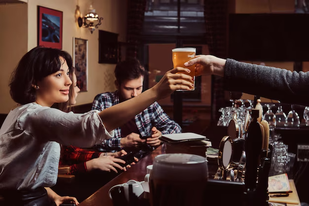 Woman receiving pint of beer at cosy pub bar, friends in background, capturing social interaction and enjoyment in local setting