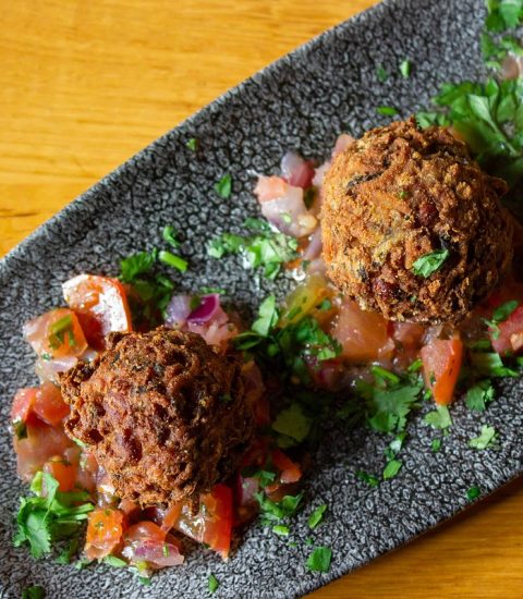 Crispy falafel balls served on a grey plate with fresh diced tomatoes and herbs, perfect for a vegetarian feast